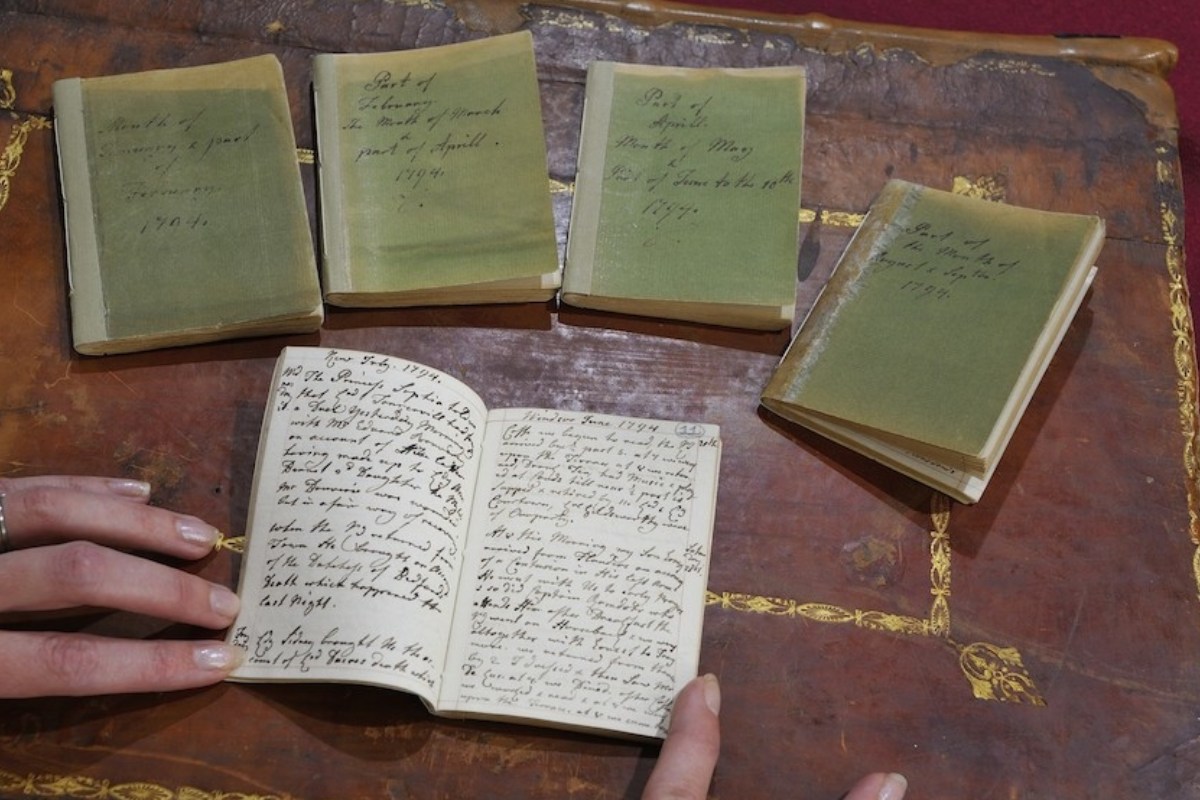 A collection of Queen Charlotte's diaries with green covers, one open to reveal handwritten entries, displayed on an ornate table.